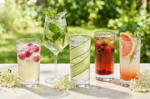 Fünf verschiedene alkoholfreie Getränke mit Holunderblüten und Minze auf einer Steinterrasse